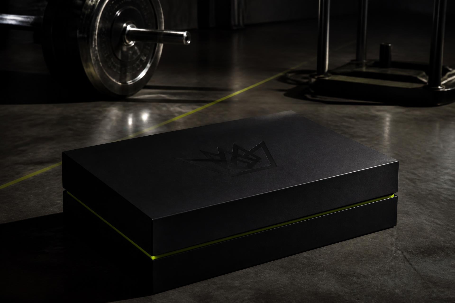 Matte black WAWDT gift box on the concrete floor of a performance gym
